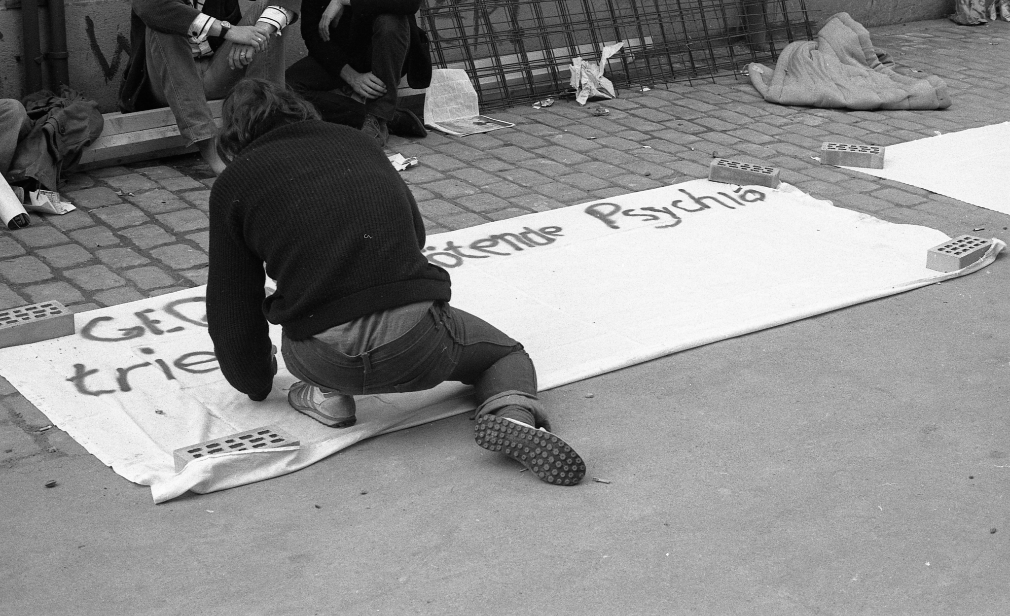 Schwarz-Weiss-Fotografie einer Person im AJZ (Autonomes Jugendzentrum Zürich), die ein Transparent mit dem Slogan "Gegen die tötende Psychiatrie" malt. Das Bild entstand 12.07.1980 und dokumentiert die Jugendbewegung der 1980er-Jahre.