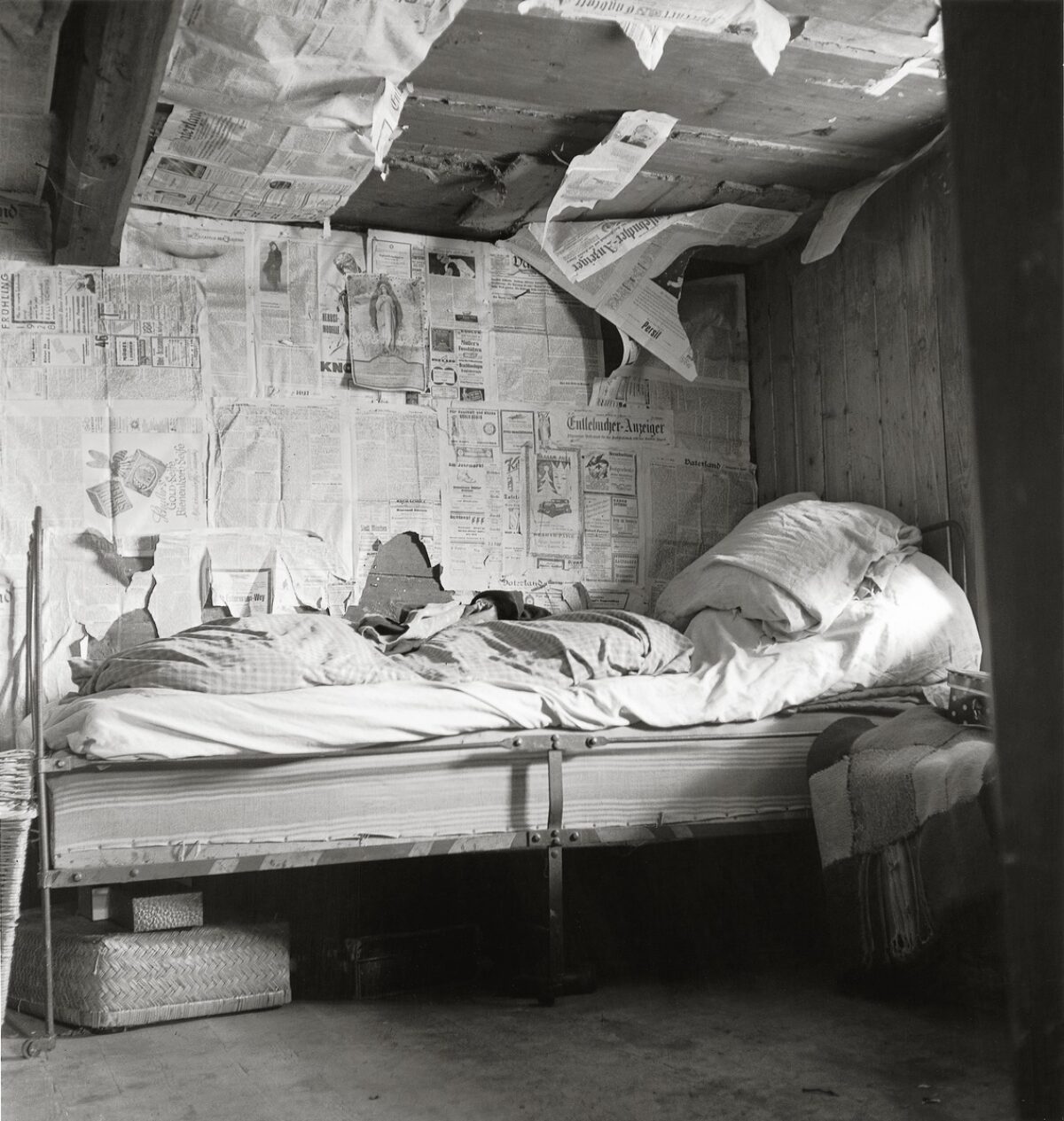 Schwarz-Weiss-Fotografie. Bett in einem Raum, der mit alten Zeitungen isoliert ist. Das Bild zeit arme Wohnverhältnisse in Flühli im Entlebuch, 1947